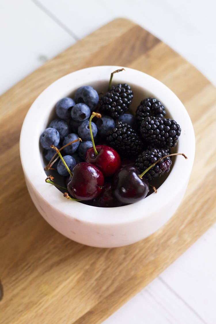 Blueberries, blackberries, and cherries in a white bowl. 