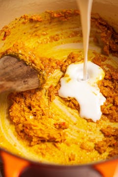 spice paste in saucepan with coconut milk being poured 