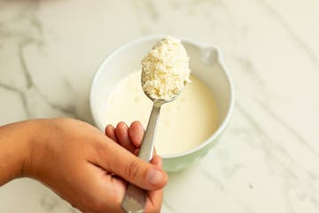 A spoonful of breadcrumbs above a bowl of cream and cheese, seasoned with salt and pepper.