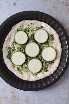 The first two pizza toppings, 6 slices of courgette are sitting on a bed of pesto. 