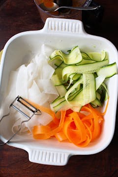 thinly sliced mooli radish, cucumber and carrot in a white dish