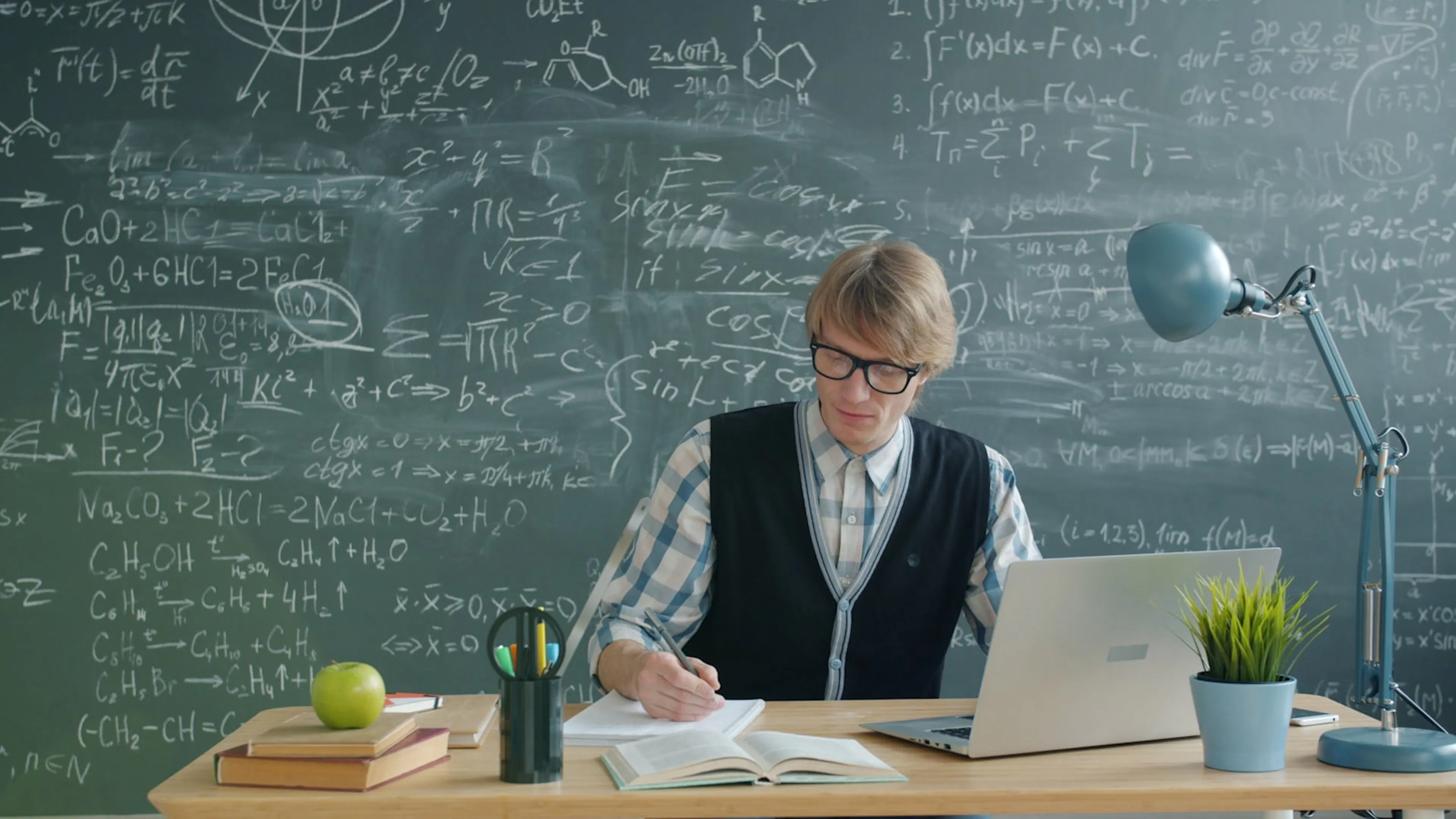 A student studying at a desk in front of a chalkboard