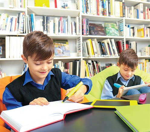 Children writing while sitting on beanbags in library