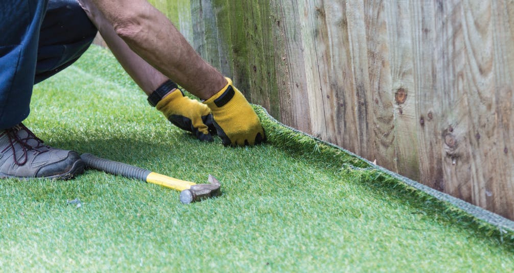 Installing artificial grass by wooden fence