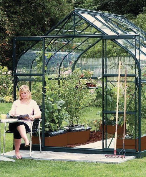 Woman sitting outside curved eave green greenhouse
