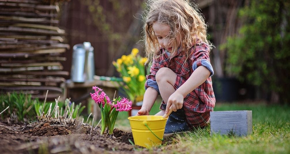 Little girl playing in garden with pot  and garden tools