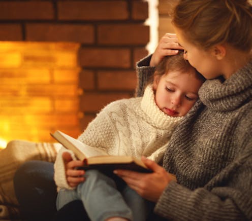 Parent and child reading in front of heater with warm glow