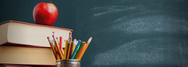 Image of a pencil cup full of pencils, a stack of books, and an apple in front of a chalkboard background