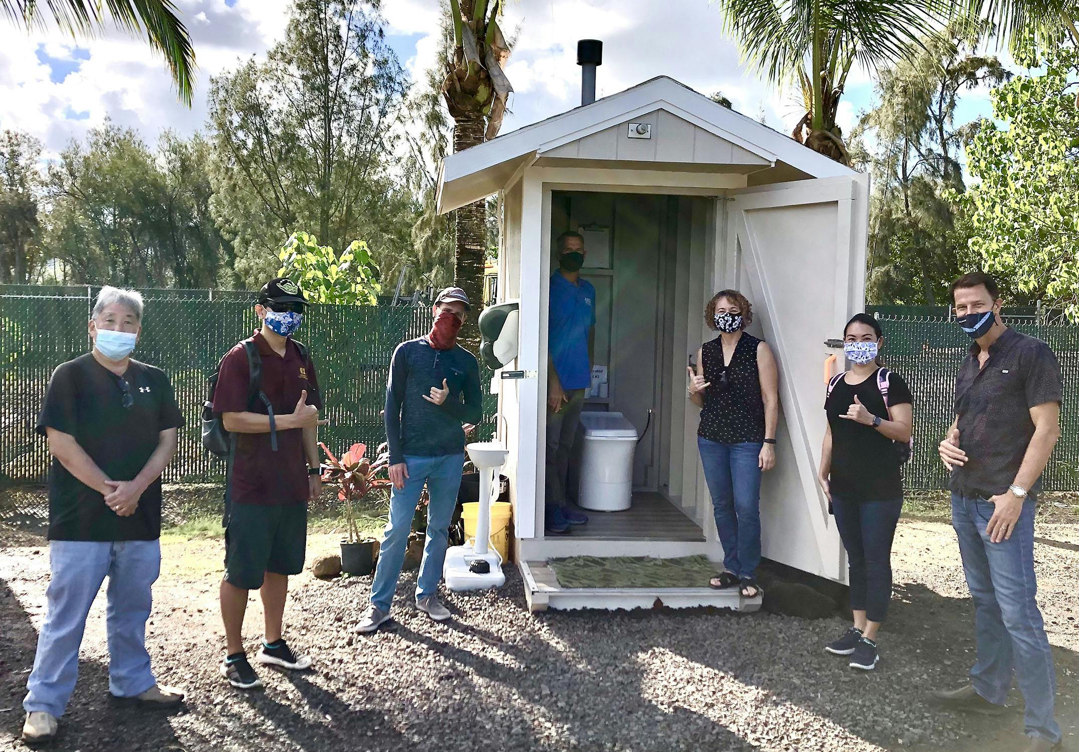 Photo of group of people standing in front of an outdoor Cinderella Incineration Toilet