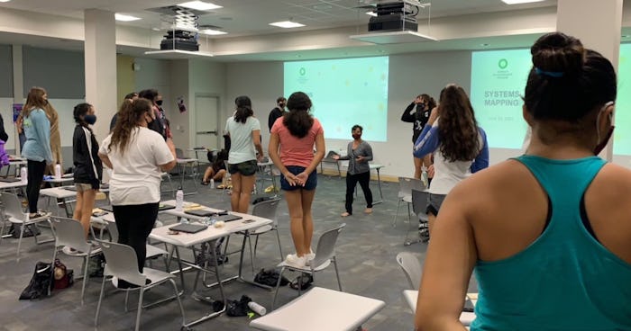 Photo of Girls in a conference room doing a group activity while standing on top of chairs.