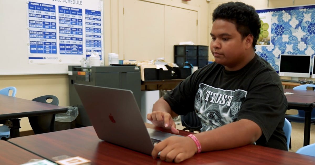 Photo of a high school student working on their laptop in a classroom.