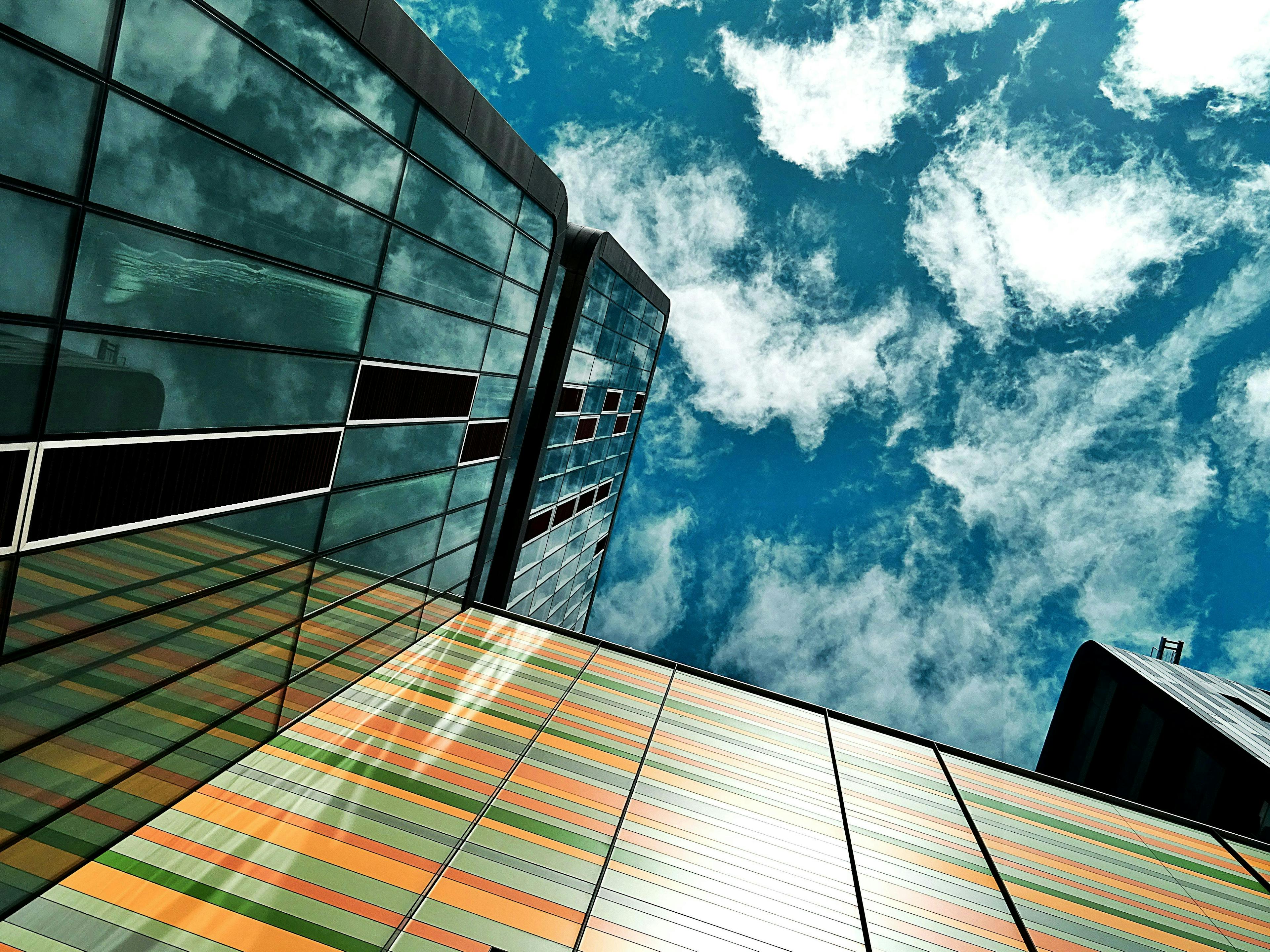 Upward view of a modern glass building with colorful panels reflecting the sky, symbolizing innovation and forward-looking architecture in business environments.
