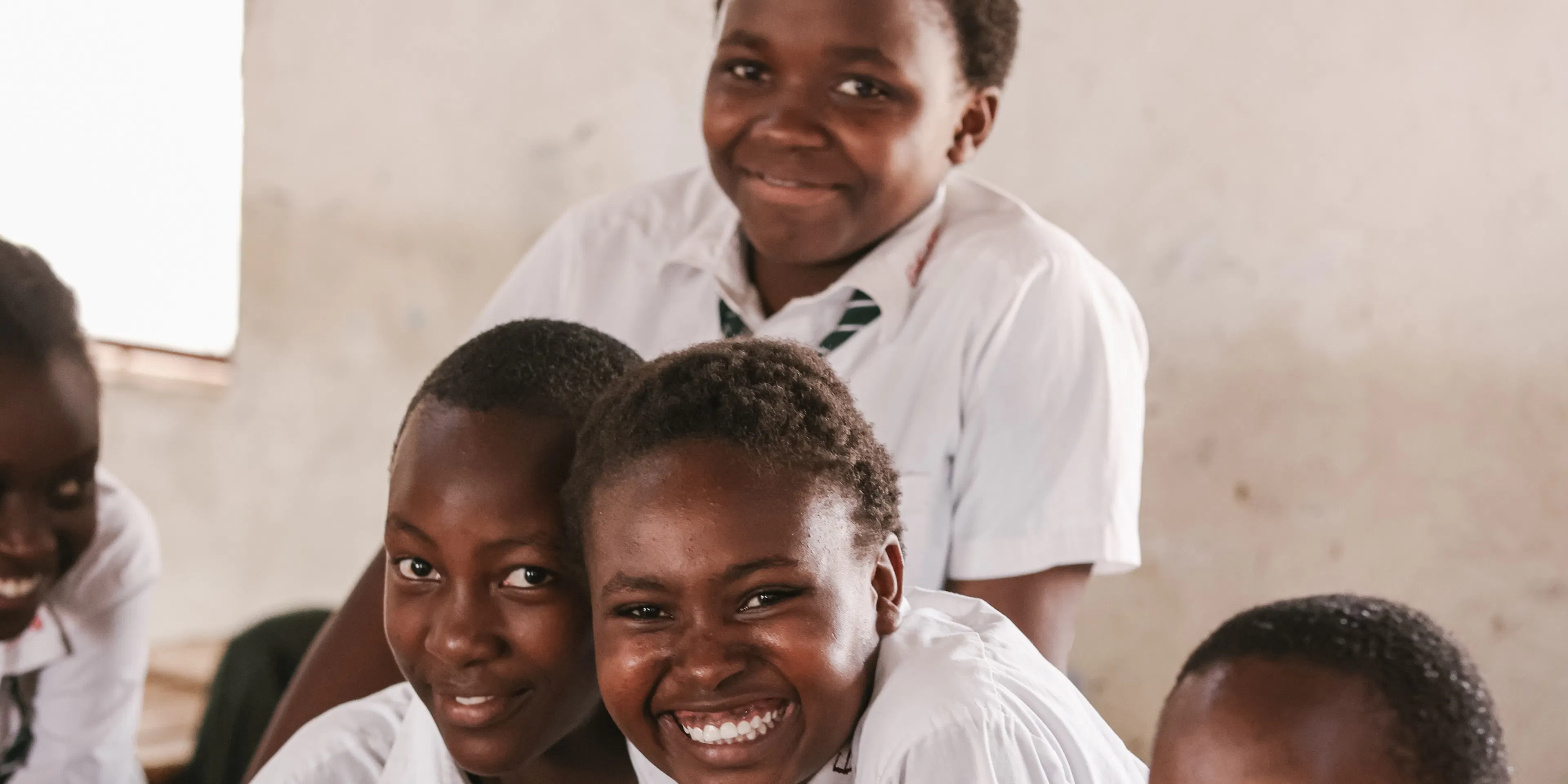 Three students smiling together at their classroom desk in Kenya