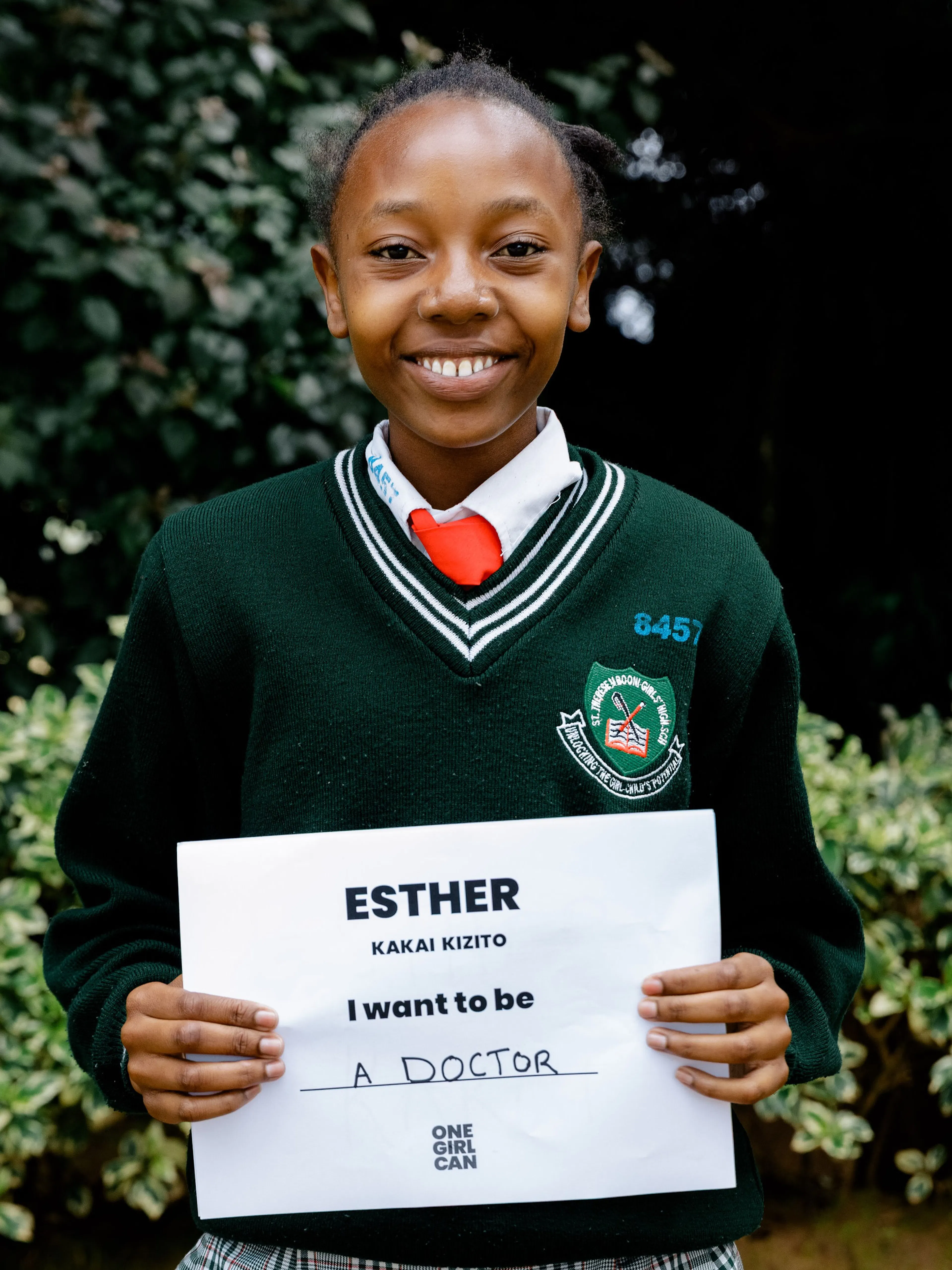 Esther, a One Girl Can scholarship candidate in school uniform, holding a handwritten sign that reads “I want to be a Doctor”
