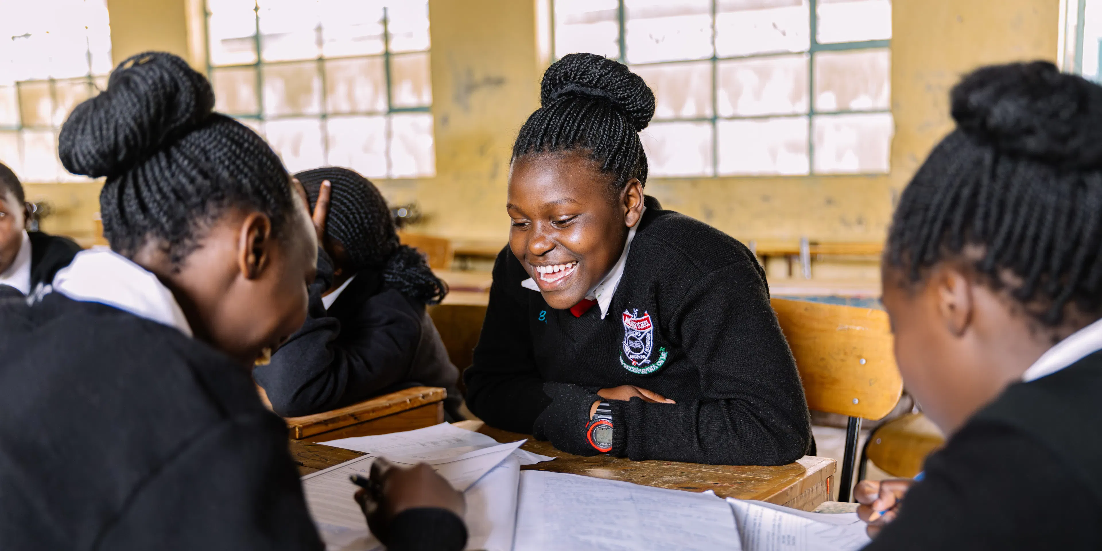 Student laughing with classmates over their work at a classroom desk in Kenya
