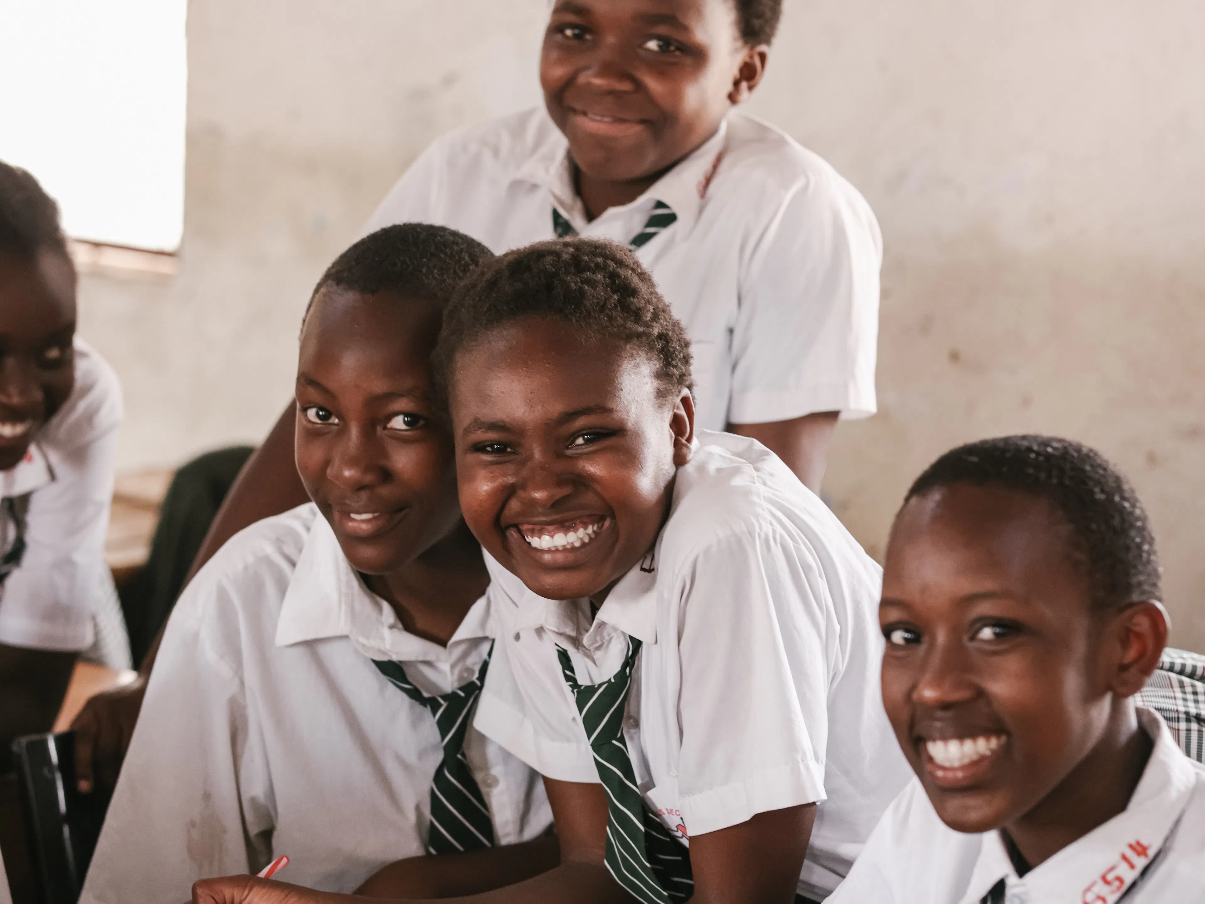 Students in white uniform shirts smiling together at their classroom desks
