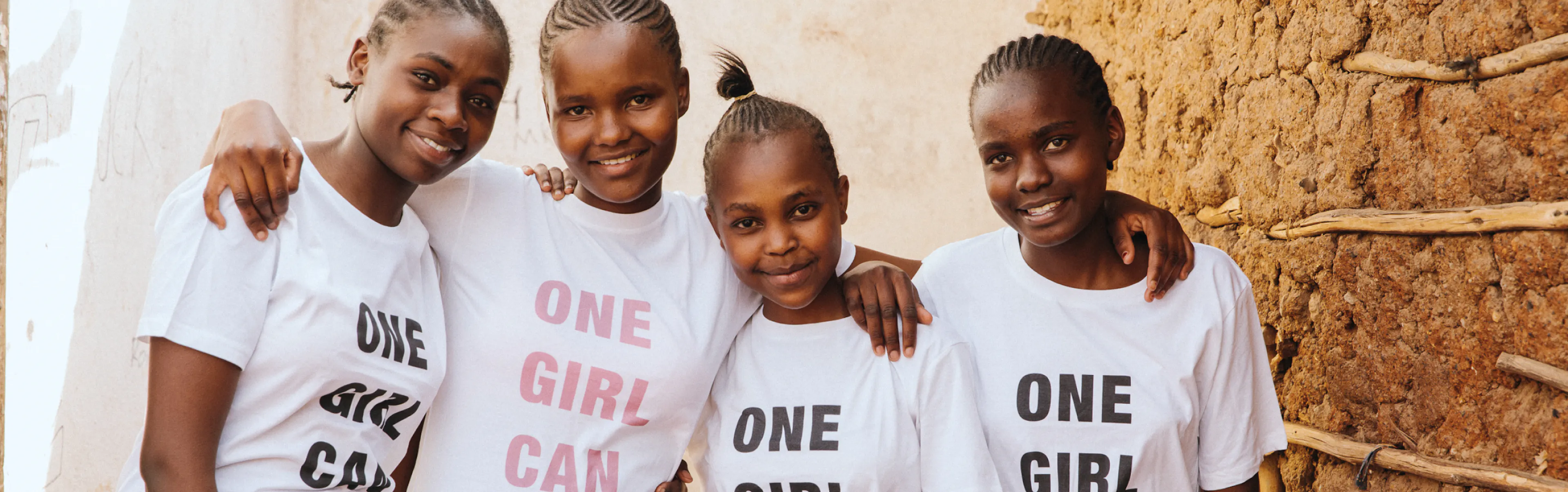 Four girls in One Girl Can t-shirts standing arm in arm outside a home
