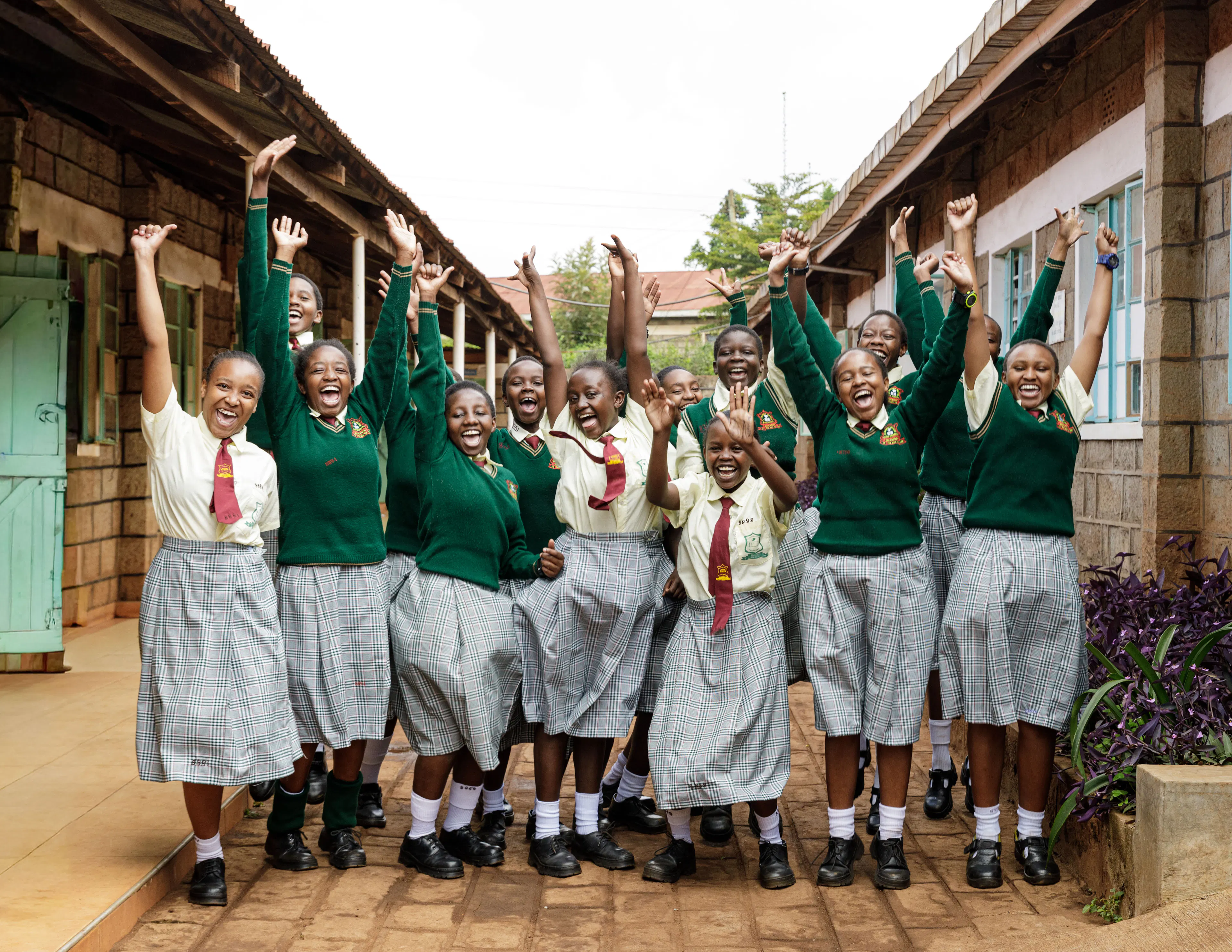 Students in green uniforms cheering with their arms raised outside their school