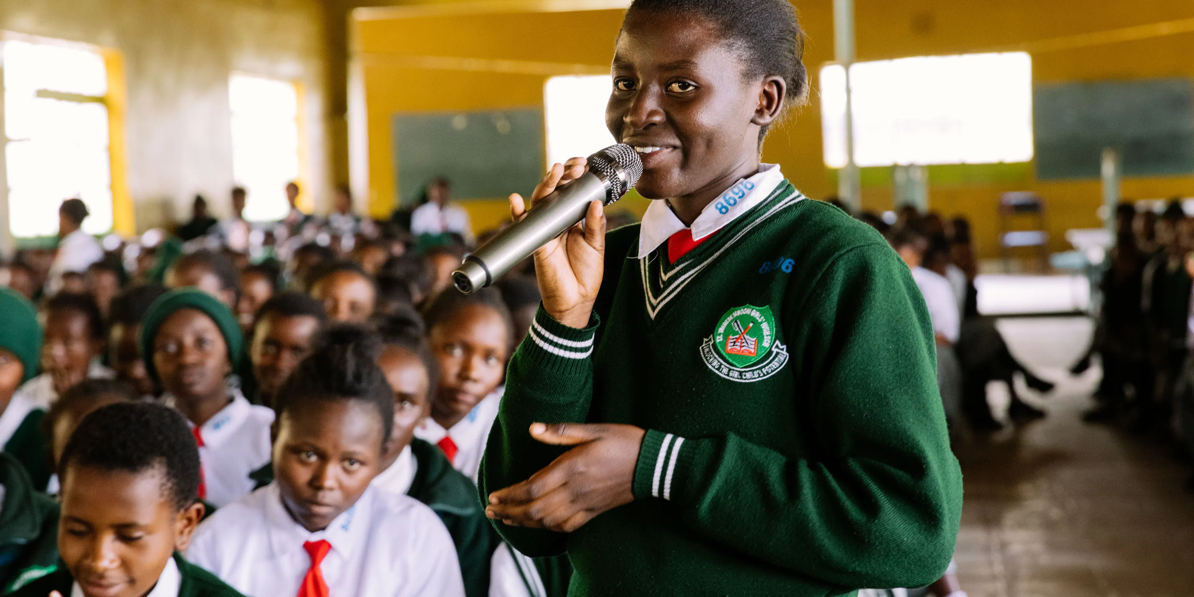Student speaking into a microphone at a school assembly in Kenya
