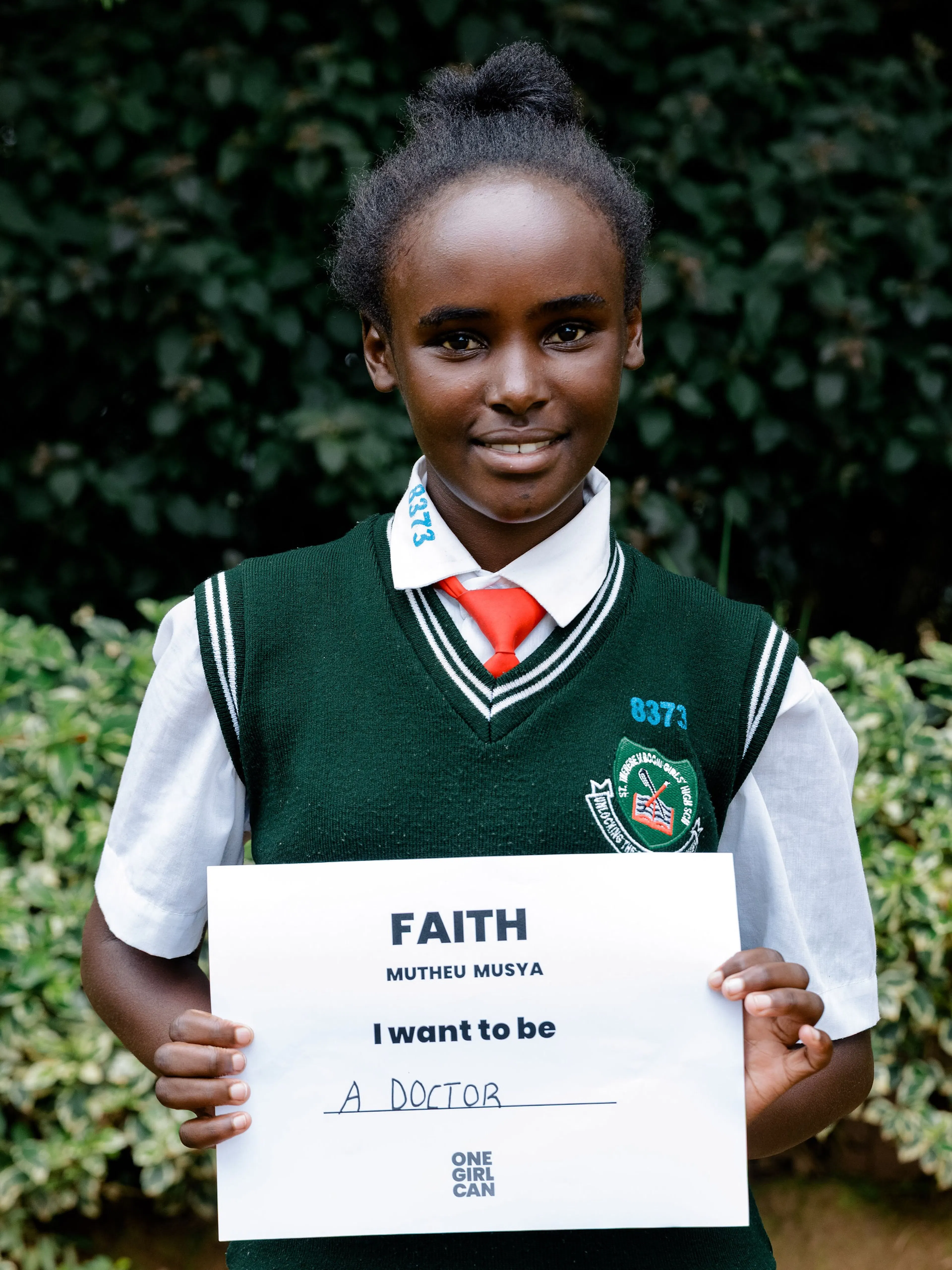 Faith, a One Girl Can scholarship candidate in school uniform, holding a handwritten sign that reads “I want to be a Doctor”