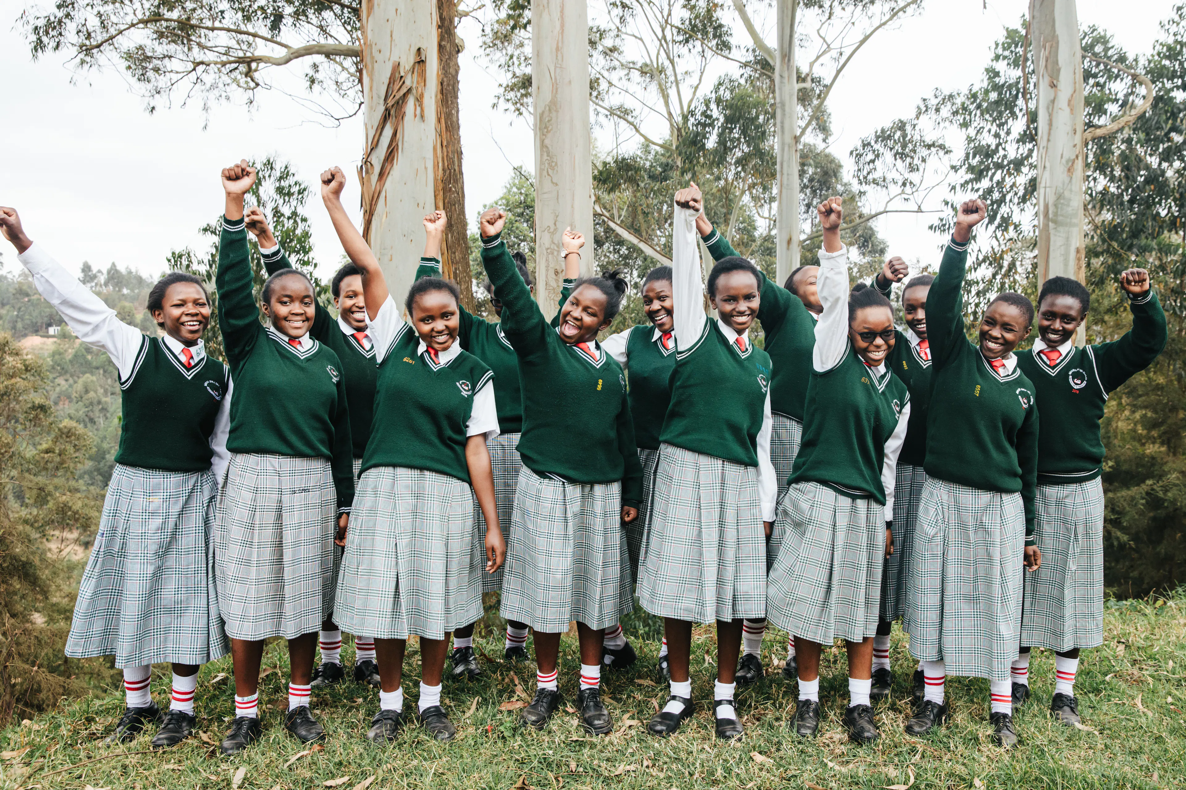 A line of students in green uniforms cheering with their fists raised in the air