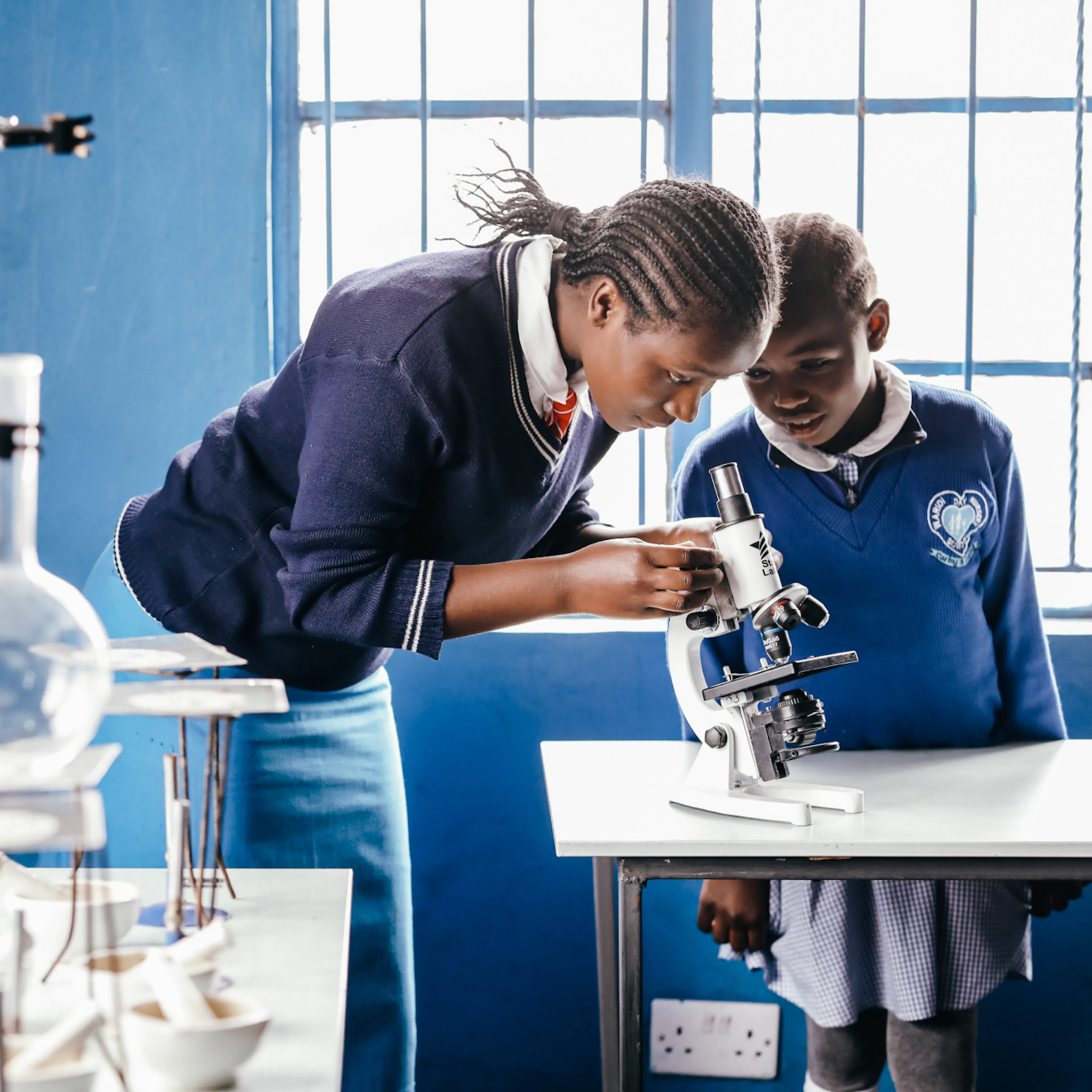 Two students examining a specimen through a microscope in a school science lab
