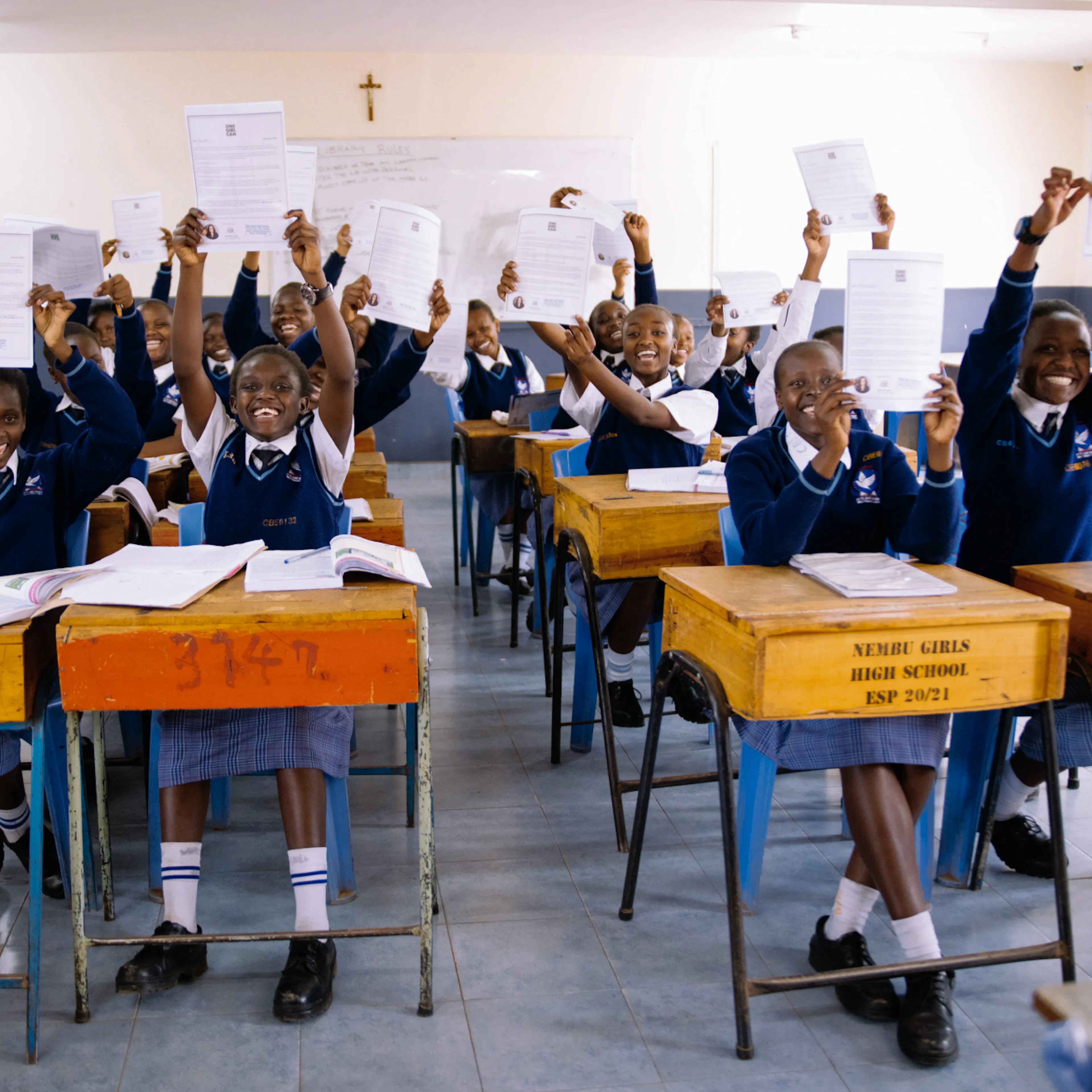 A classroom of students in navy uniforms cheering with their exam papers raised