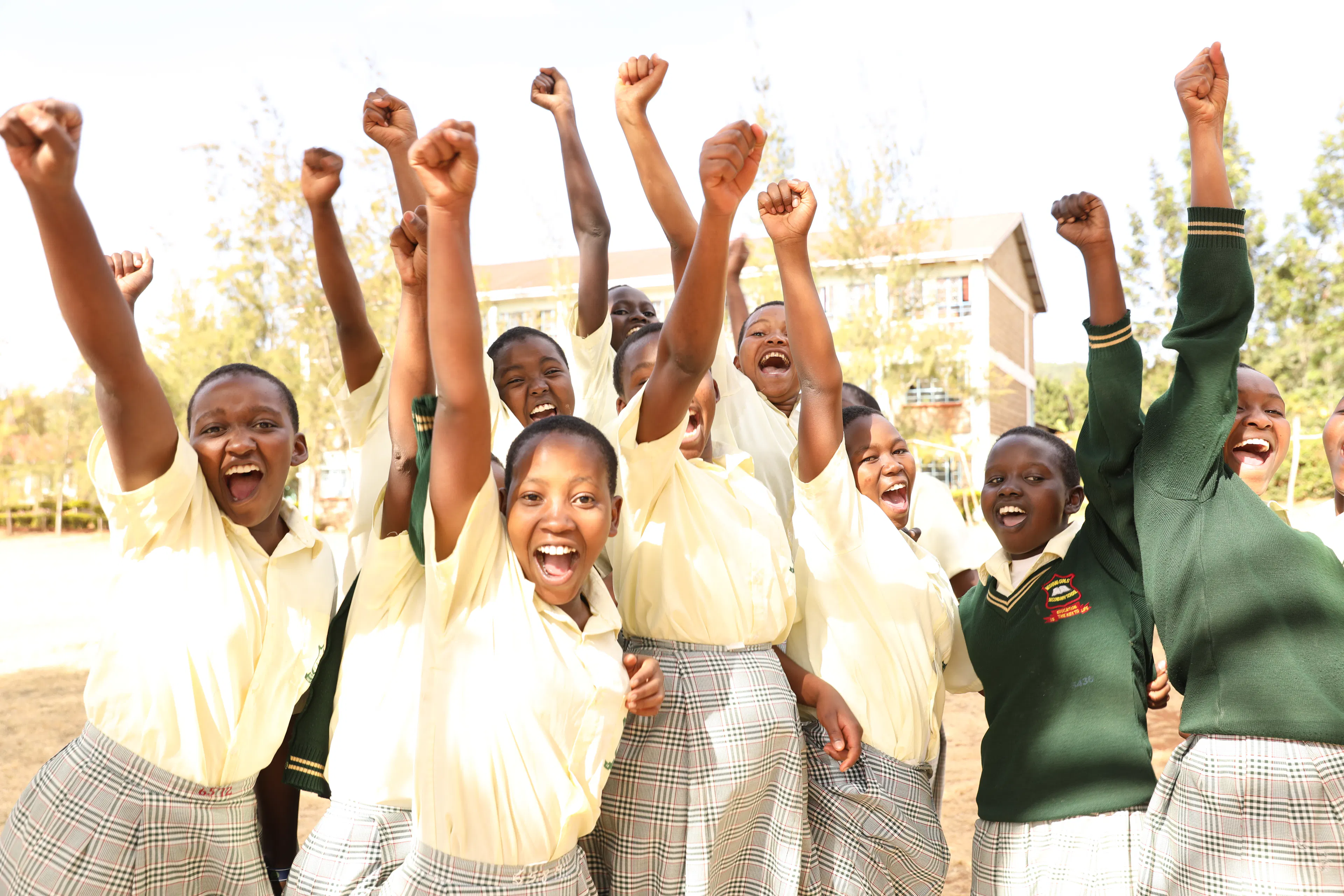 Students in yellow and green uniforms cheering with their fists raised