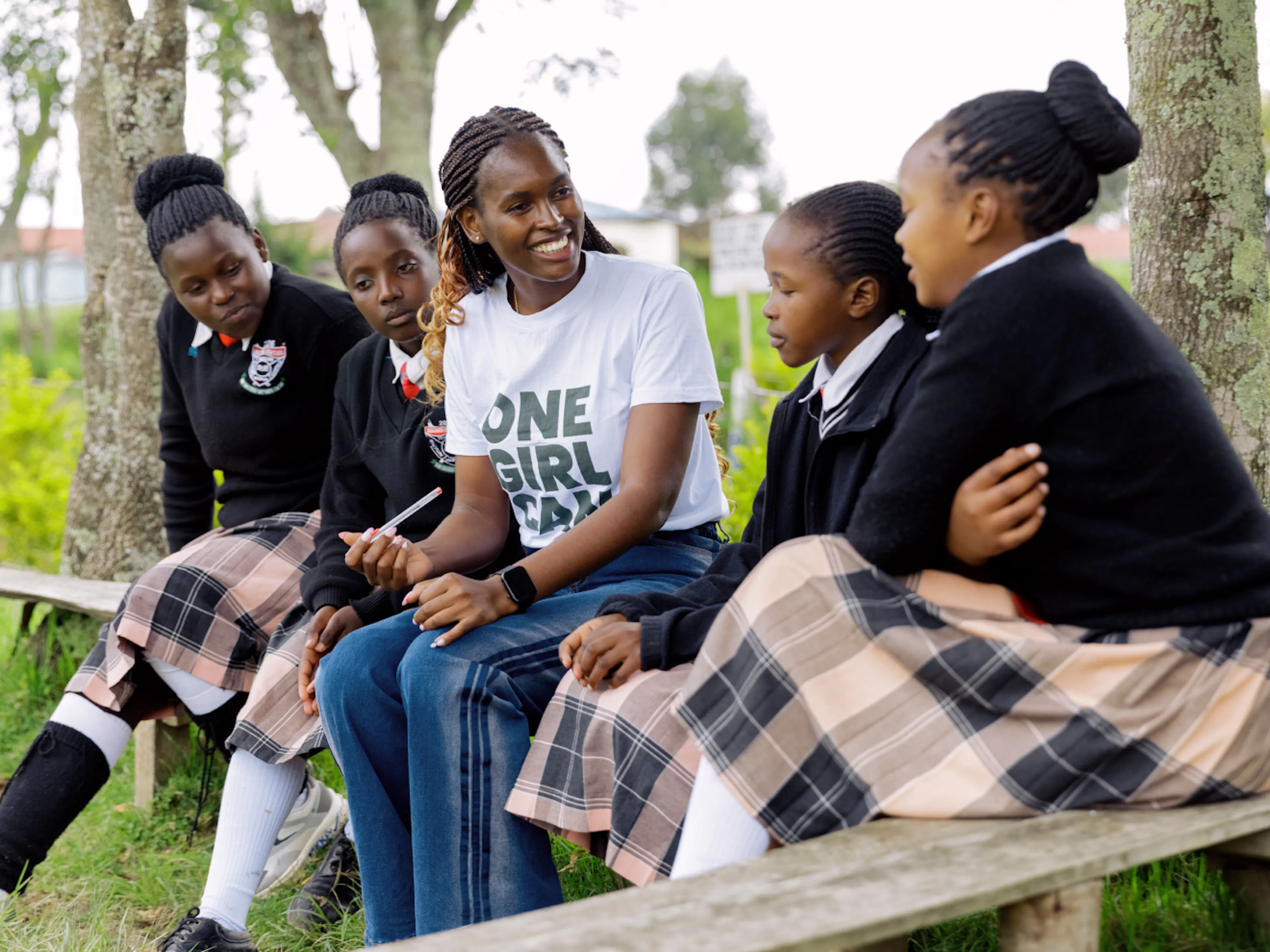 A One Girl Can mentor talking with four high school students on a bench outdoors
