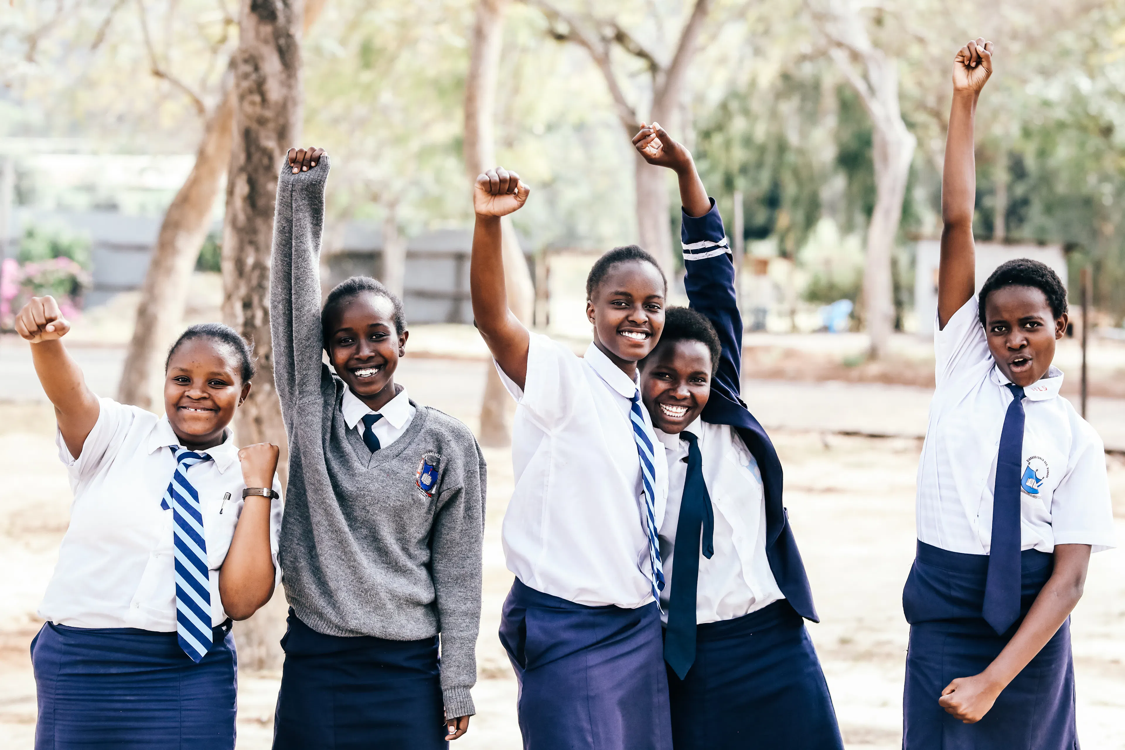 Five One Girl Can students in school uniforms cheering with their arms raised