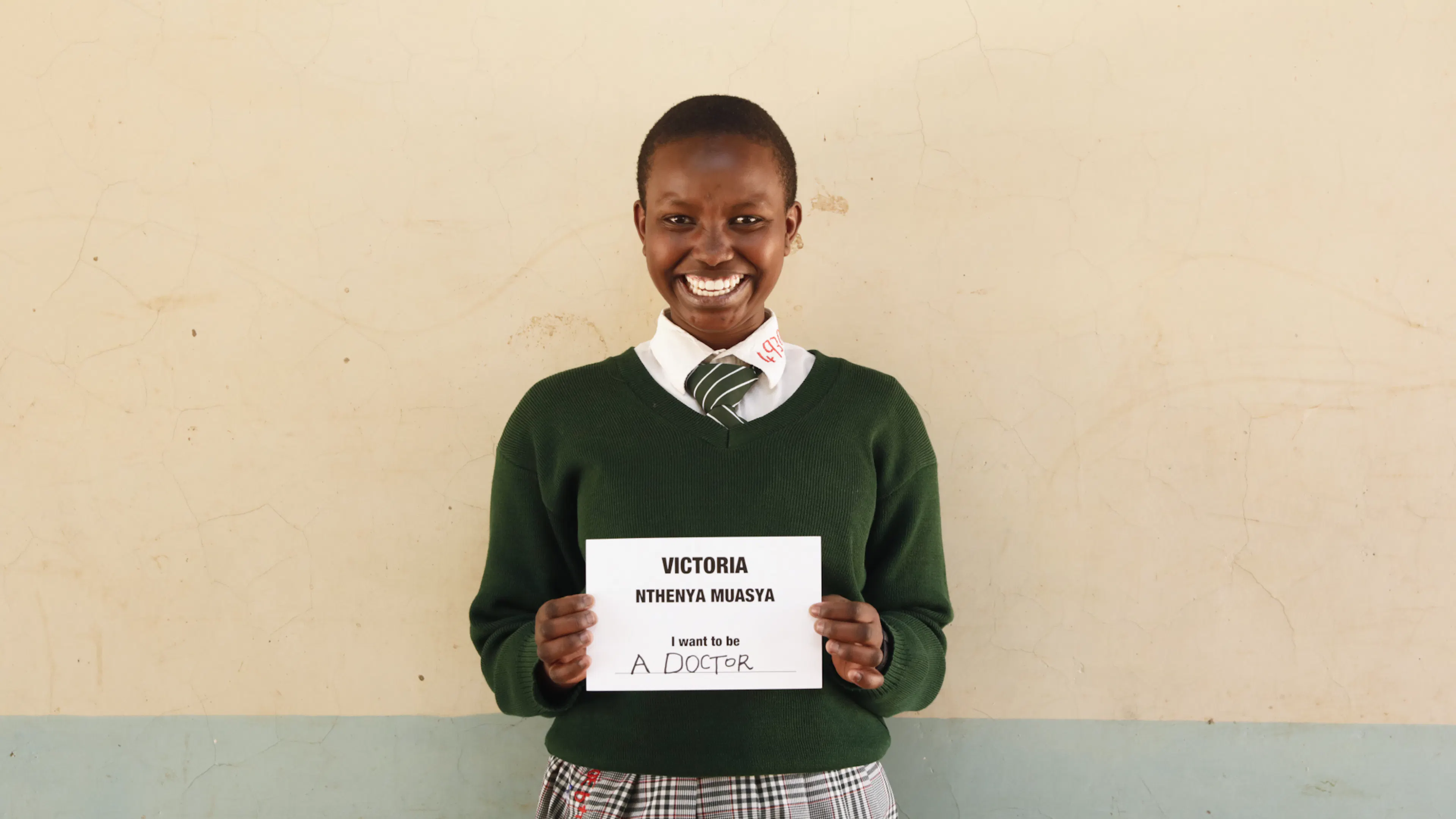 A student holding a handwritten sign reading 'Victoria - I want to be a doctor'