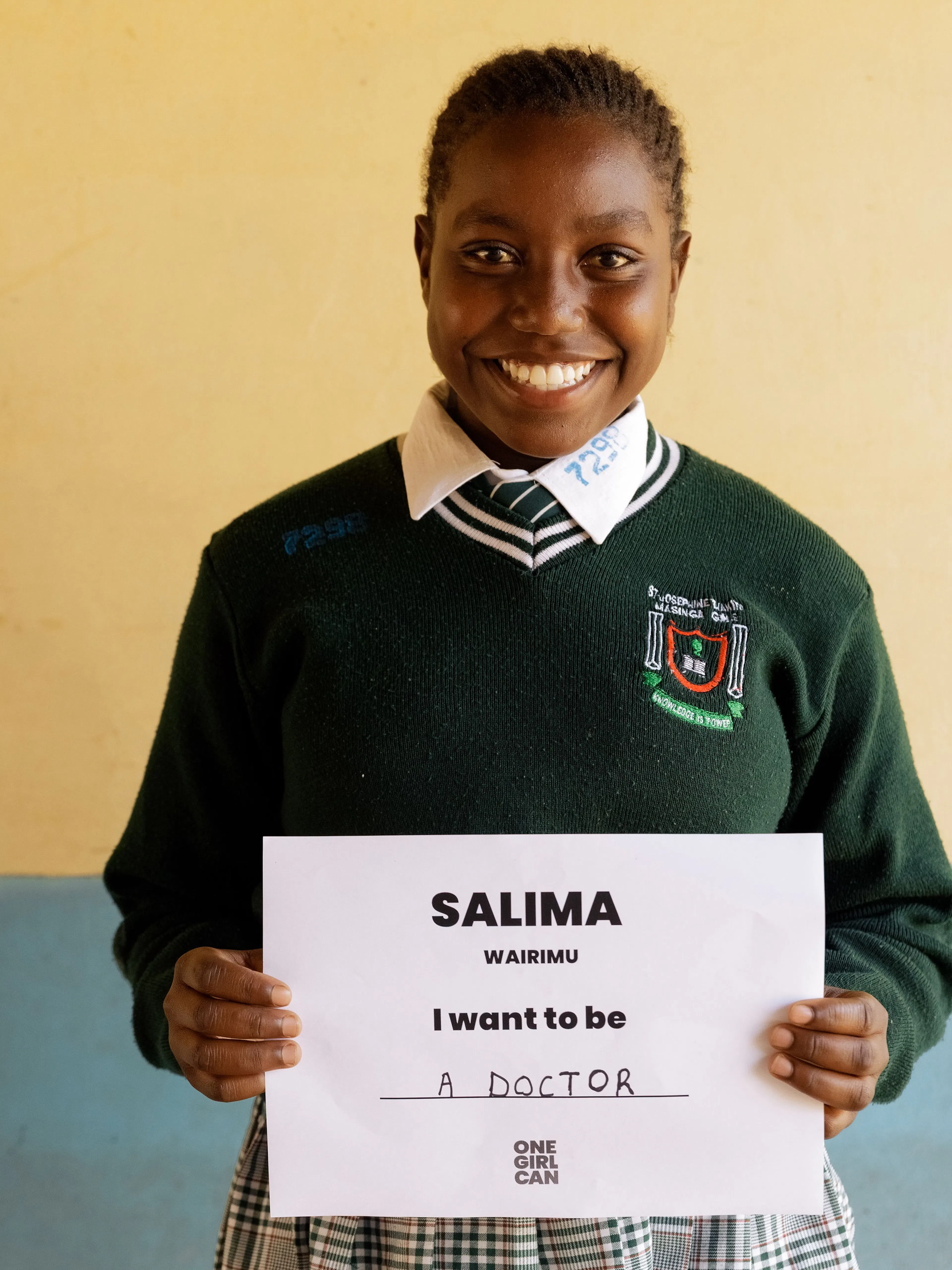 Salima, a One Girl Can scholarship candidate in school uniform, holding a handwritten sign that reads “I want to be a Doctor”