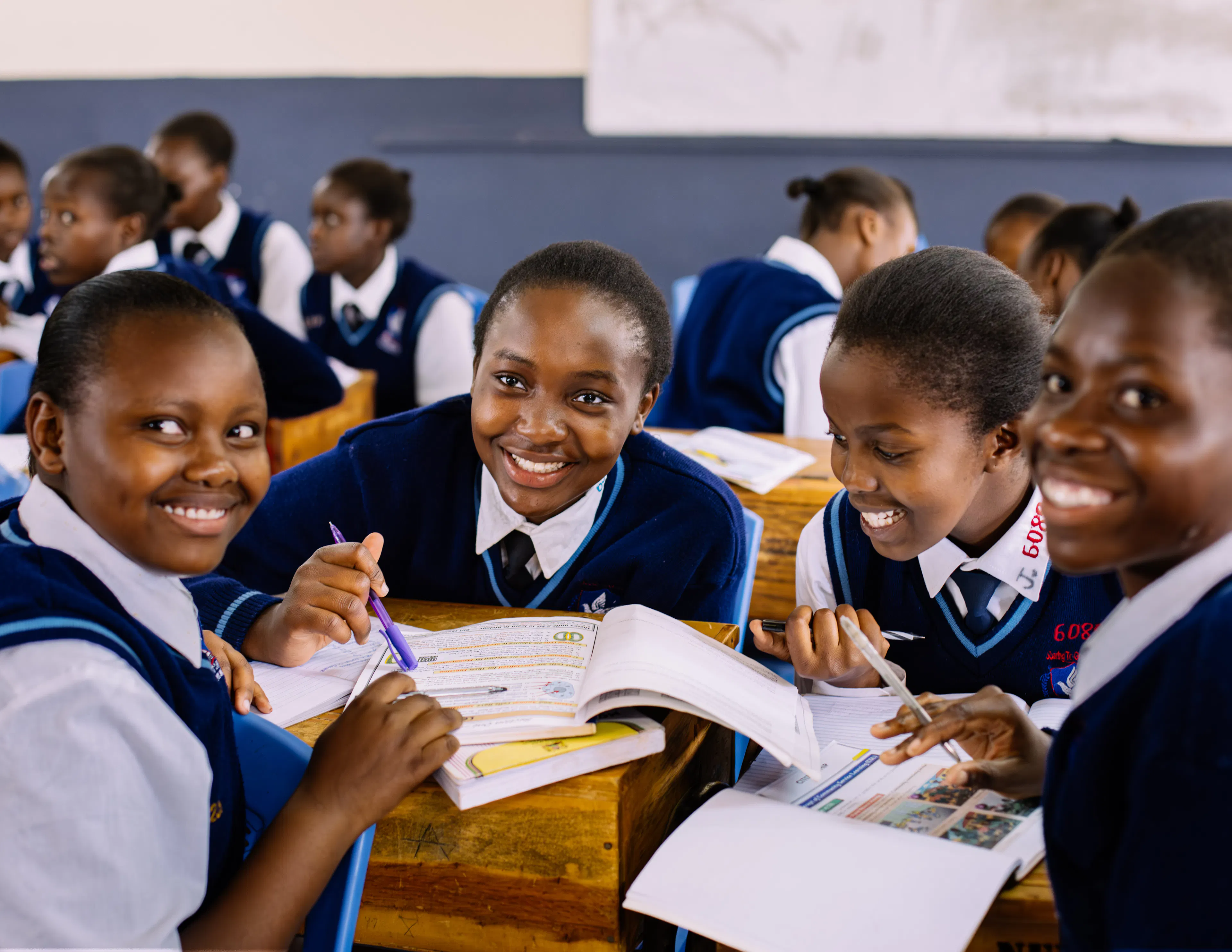 Four students in navy uniforms sharing textbooks at their desks in a classroom