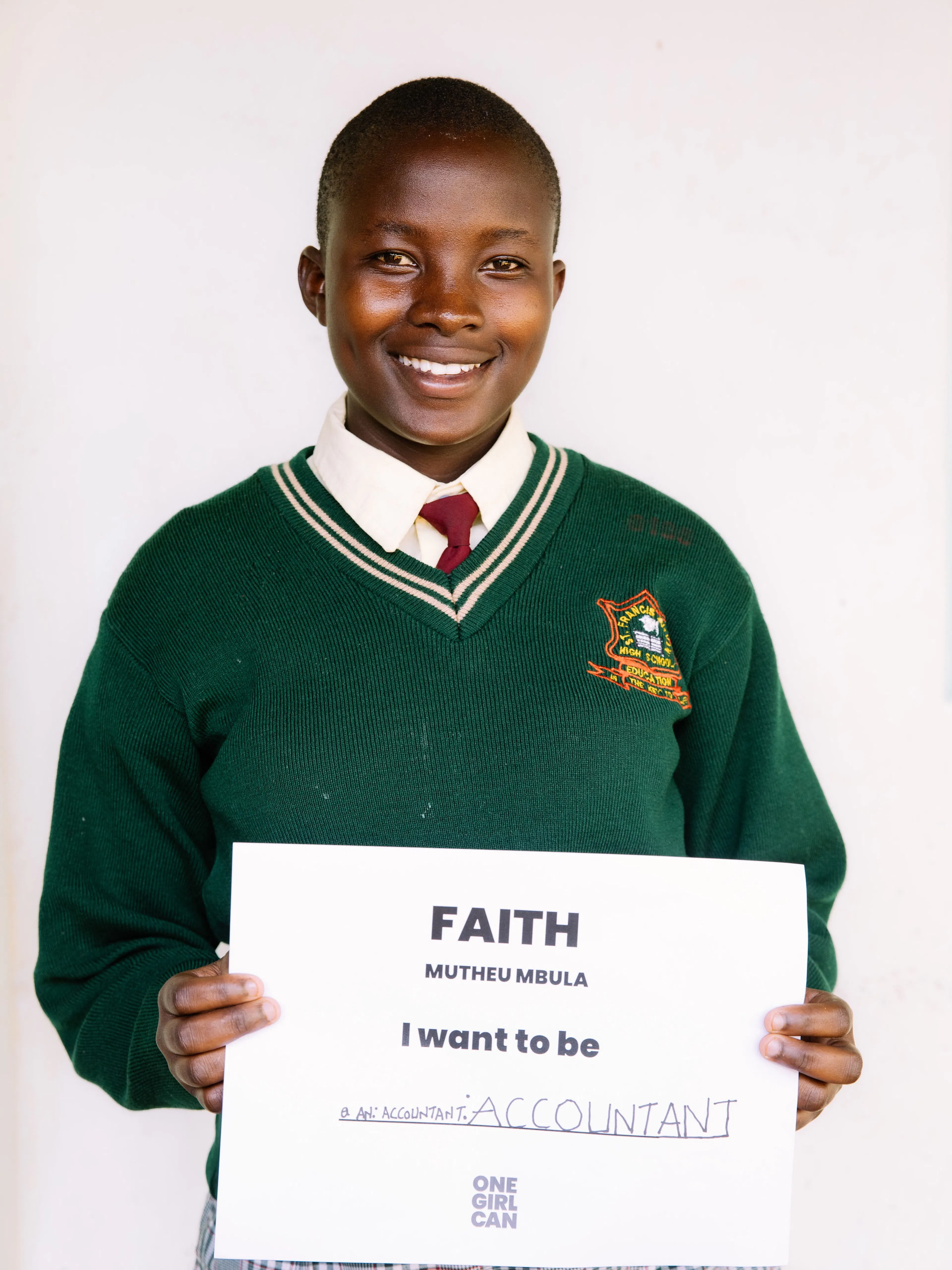 Faith, a One Girl Can scholarship candidate in school uniform, holding a handwritten sign that reads “I want to be an Accountant”