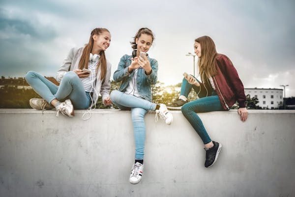  Tre jenter med hver sin mobiltelefon sitter på en murvegg. 