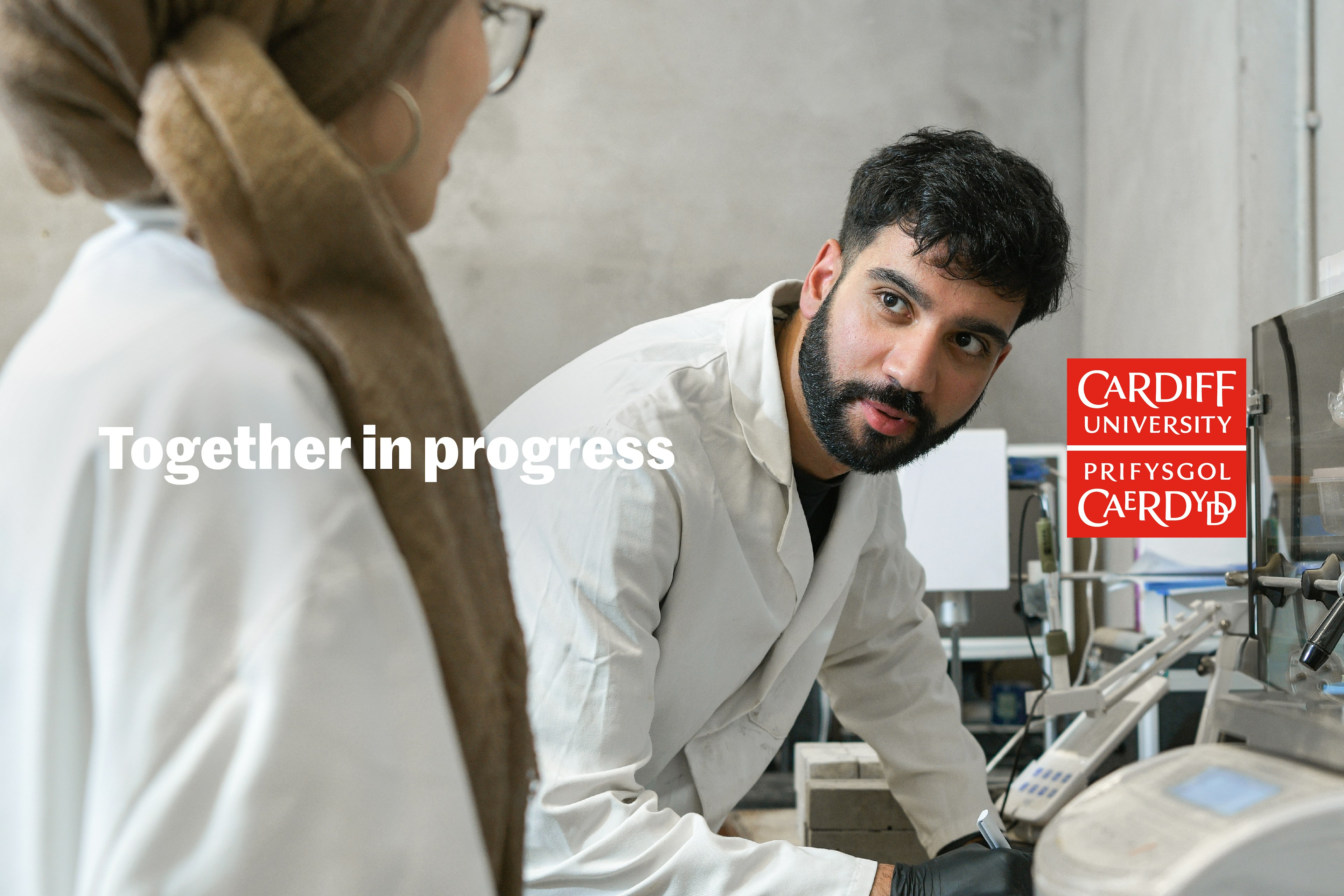 Students in white lab coats collaborating on a piece of work, surrounded by machinery.