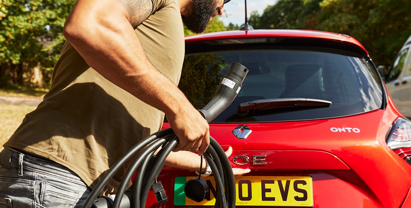 Man with electric charging cable in his hand, as he reaches for the boot of a Renault Zoe