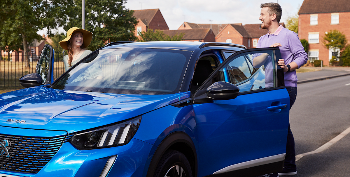 A man and woman smiling as they stand by the open doors of a blue Peugeot 2008