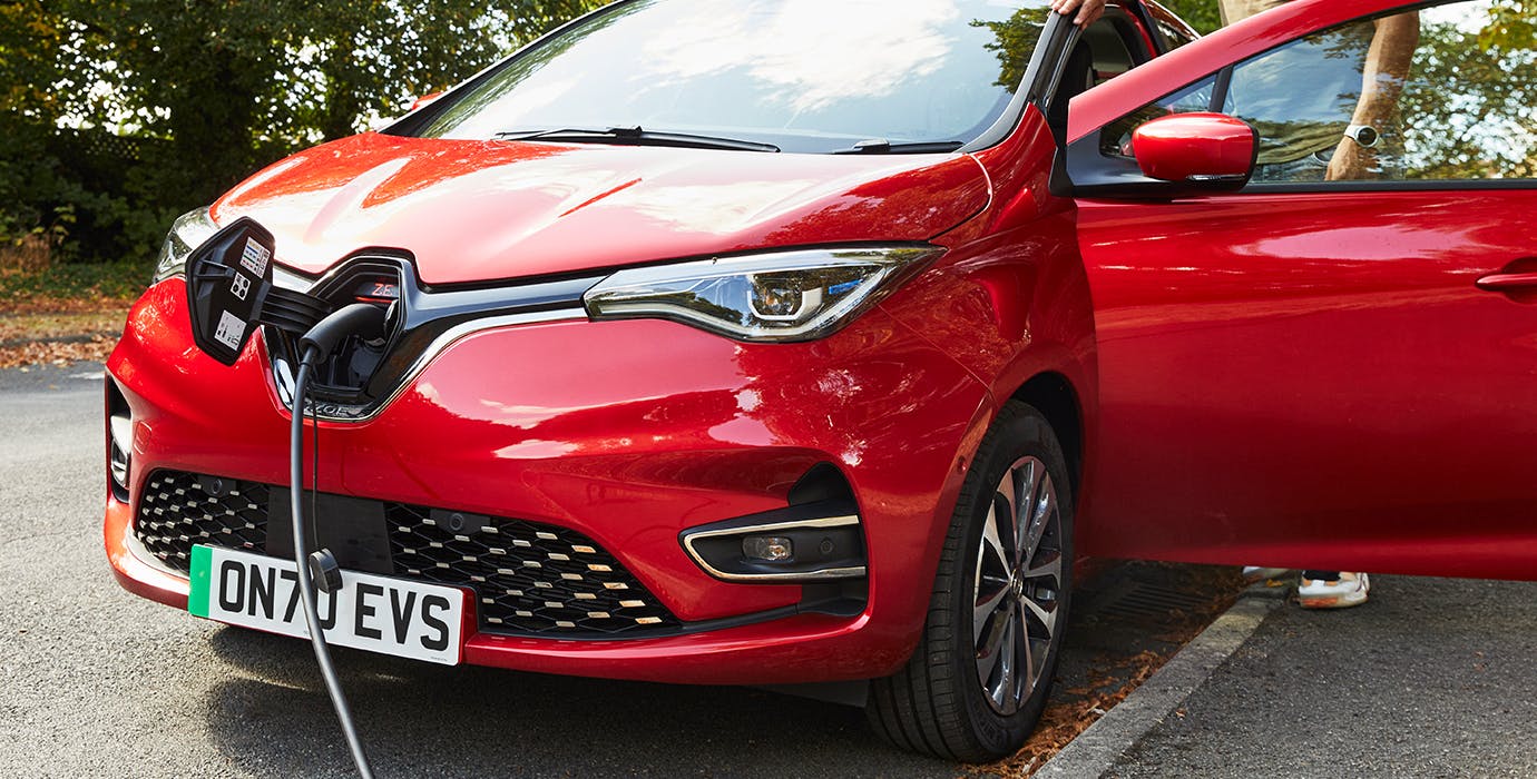 A red Renault Zoe parked by the side of the road, with an electric charger plugged in the front of it