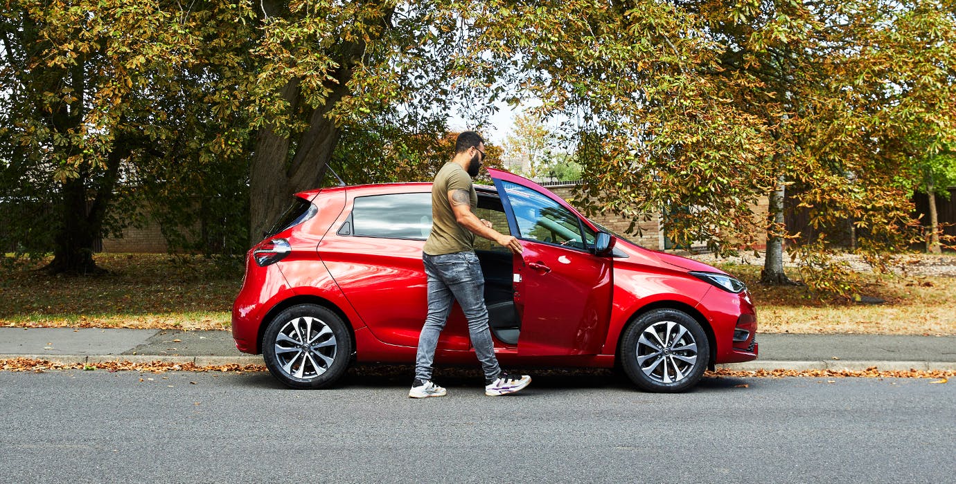 Man entering the driver's seat of a red Renault Zoe. There is a back-drop of trees.