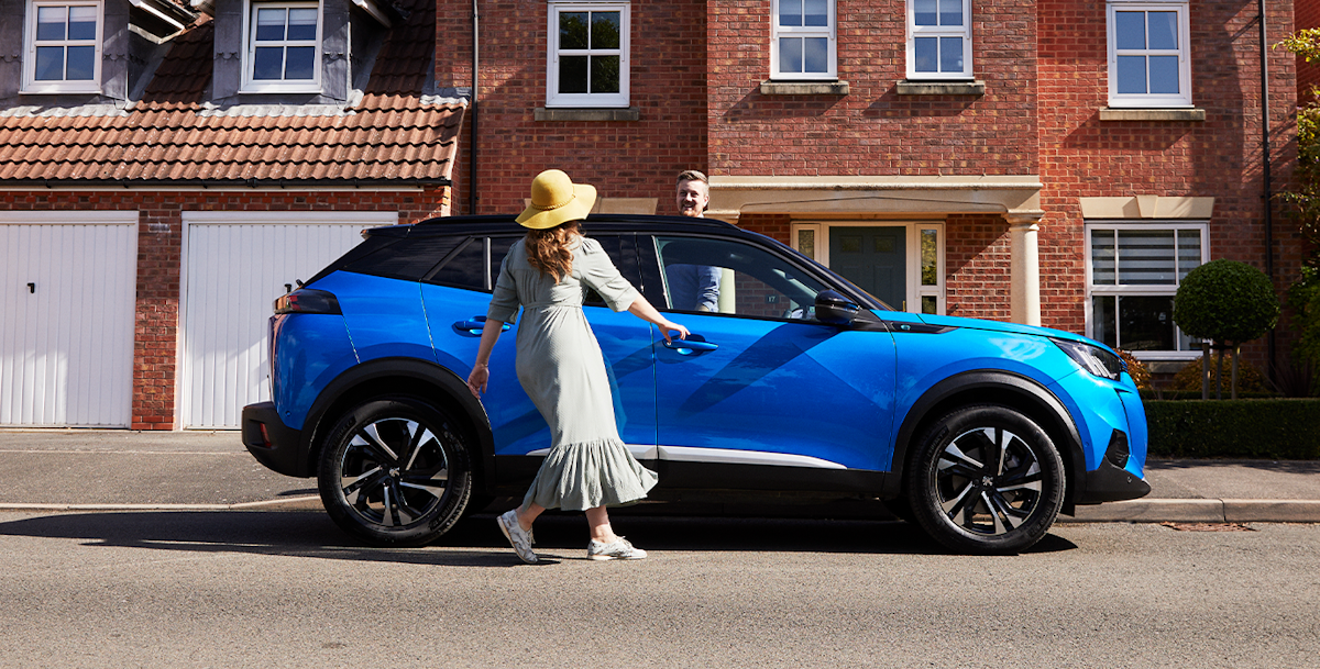 Woman walking up to the driver's door of a blue Peugeot 2008