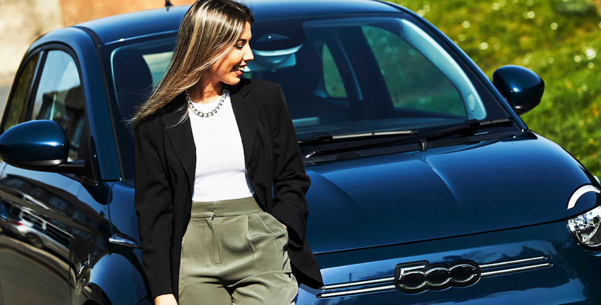 Woman looking happy, leaning on the bonnet of a blue Fiat 500 hatchback