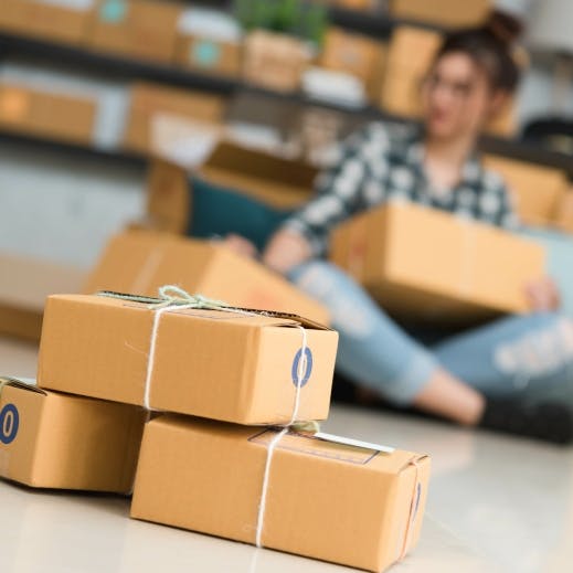 Student wearing jeans and a trendy blue check shirt sits on the floor and sorts through parcels