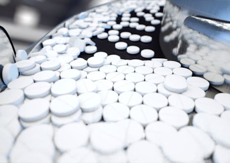 White medicine pills coming out of a machine in a pharma factory.
