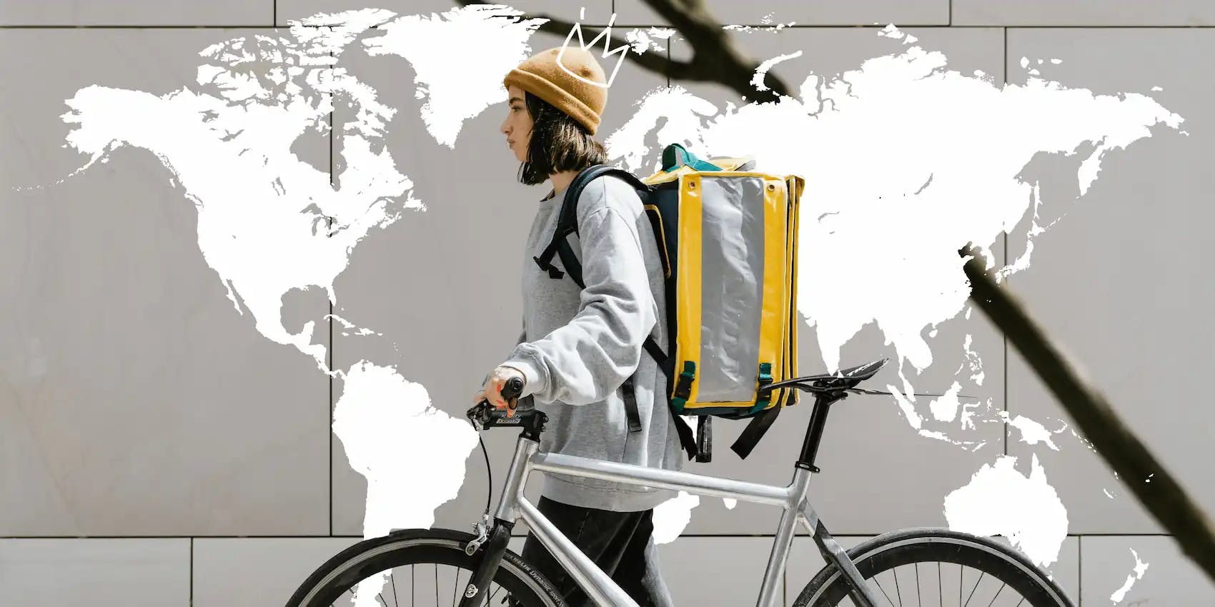 Dünya haritalı kapının yanında bisikletiyle yürüyen sırt çantalı bir kız.