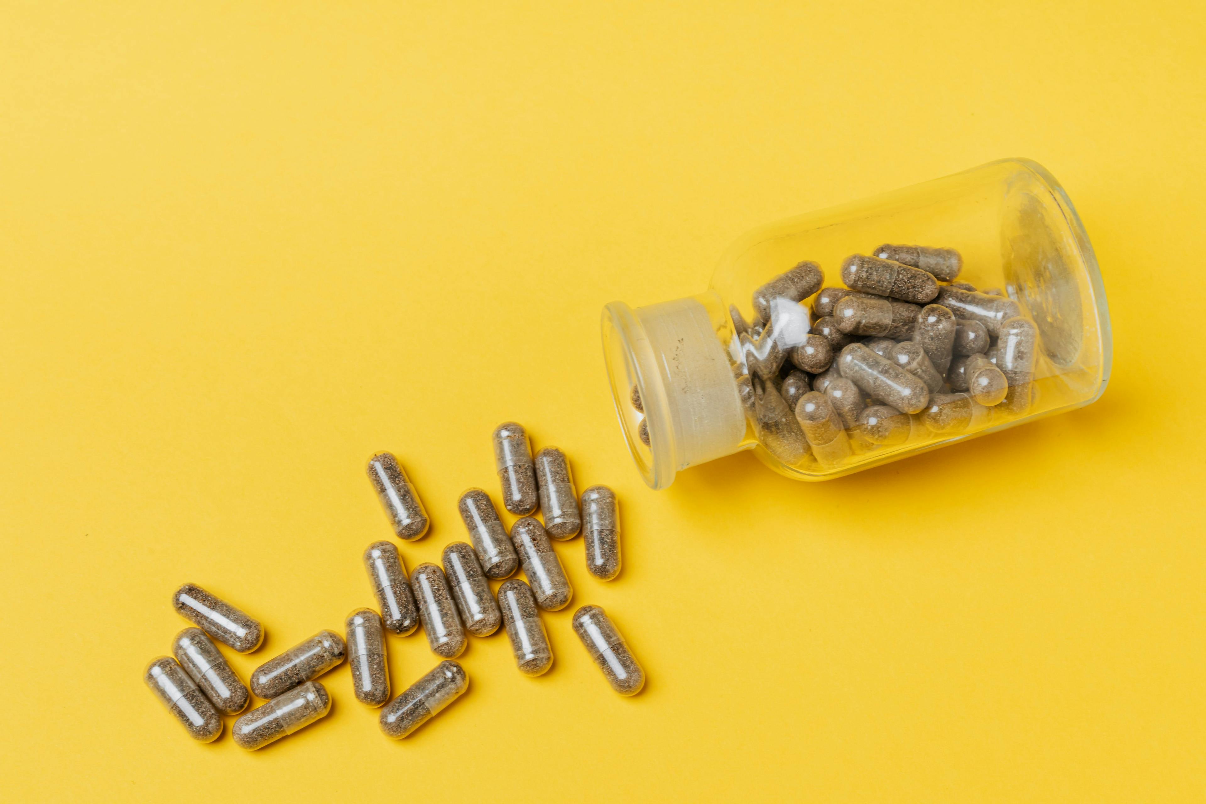 Medical supplements in capsule form spilling from glass bottle on yellow background