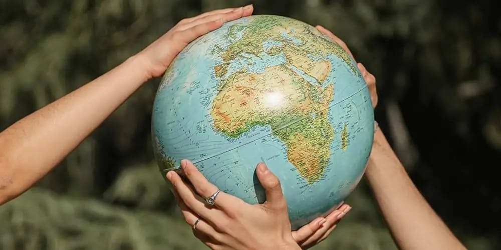 Minyatür bir dünya küpünü tutan dört el.