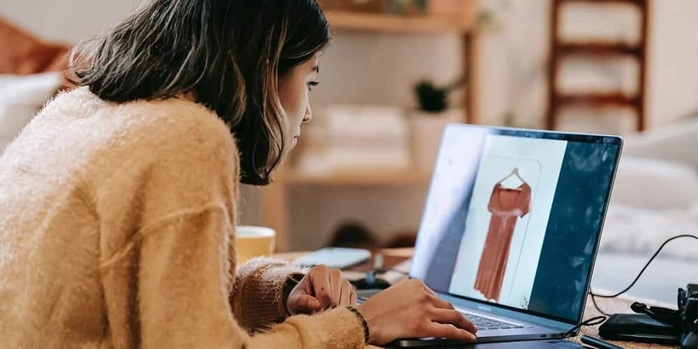 Bir kadın dizüstü bilgisayarıyla internette geziniyor ve kırmızı bir elbiseye bakıyor.