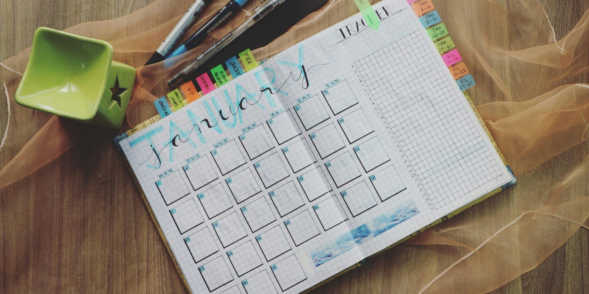 January planner calendar page with colorful tabs and green star bowl on wooden desk