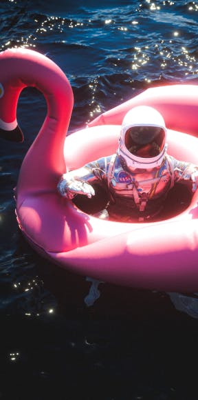 Astronaut floating on pink flamingo pool float at night